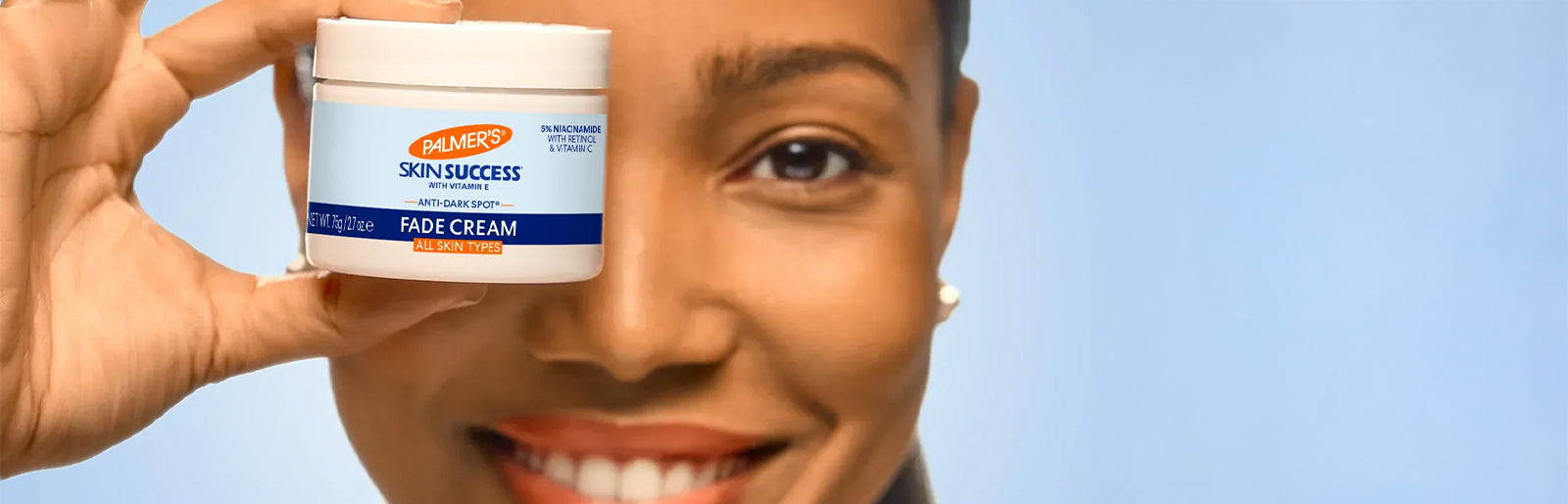 Close up of woman holding jar of Palmer's Skin Success Fade Cream in front of her eye